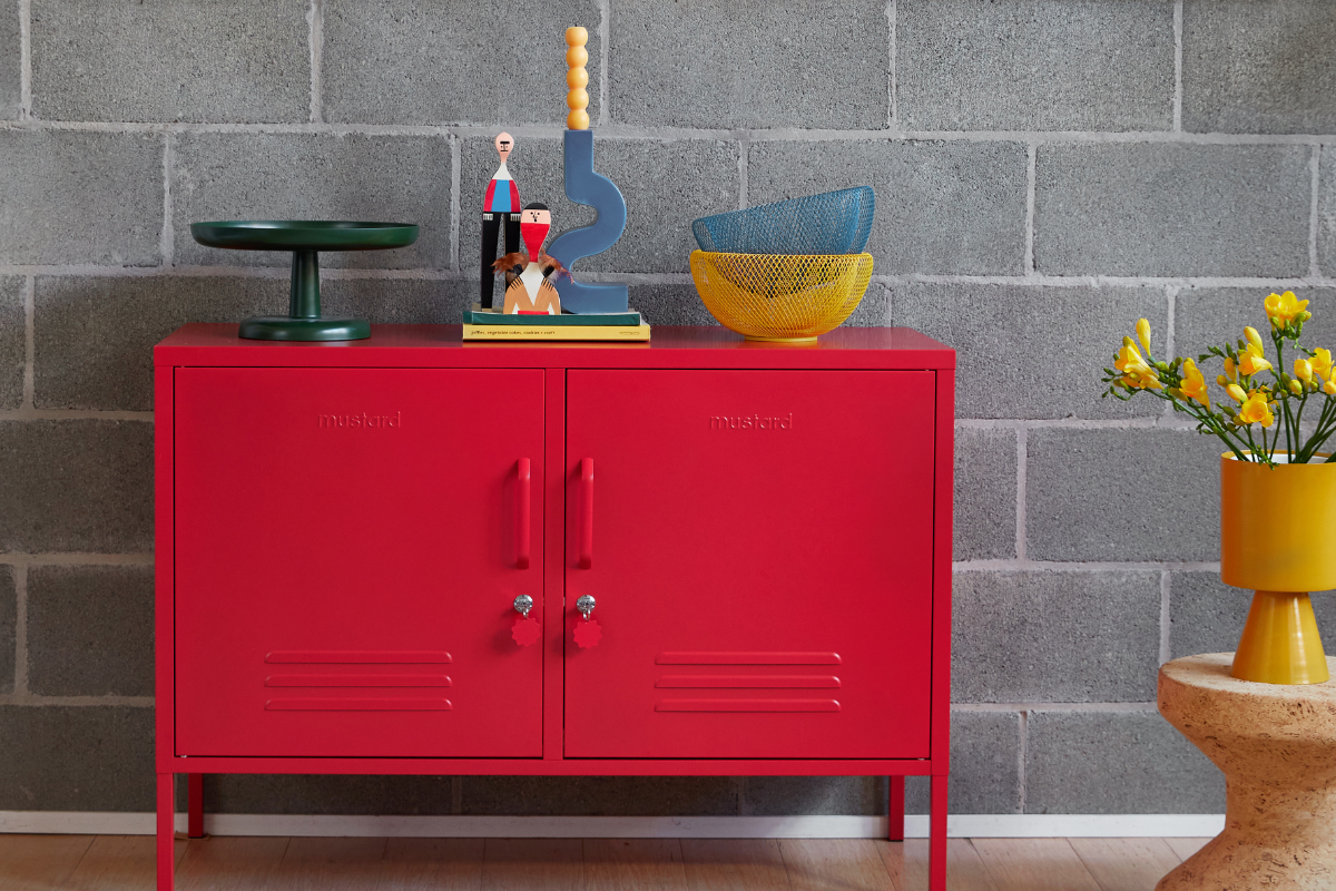 A Poppy Lowdown sits in front of a grey wall with monochrome art work hung on it. A vase of yellow flowers sits next to it and blue and yellow accessories decorate the top.
