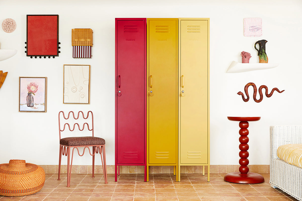 The Skinny lockers in Poppy, Mustard and Butter lined up against a gallery wall with a wavy chair and side table