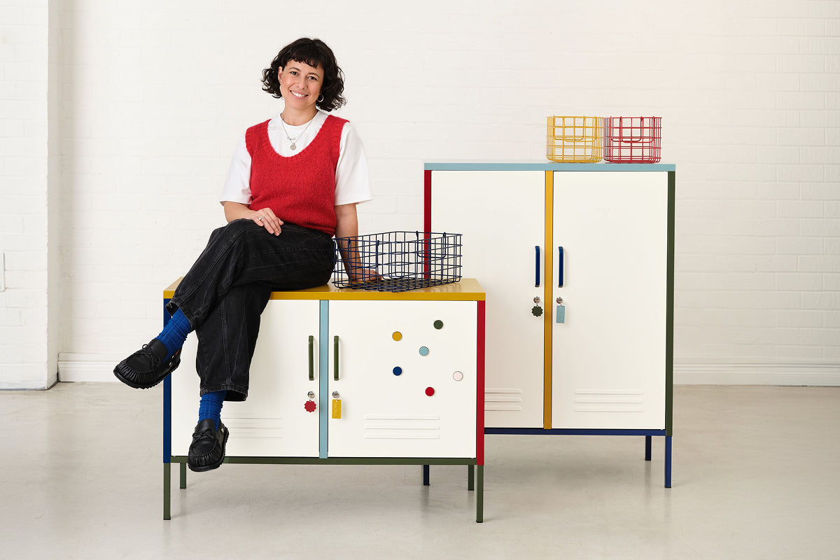 Becca seated on The Lowdown locker beside The Midi, styled with wire Baskets and Buttons in the Mustard x MoMA palette