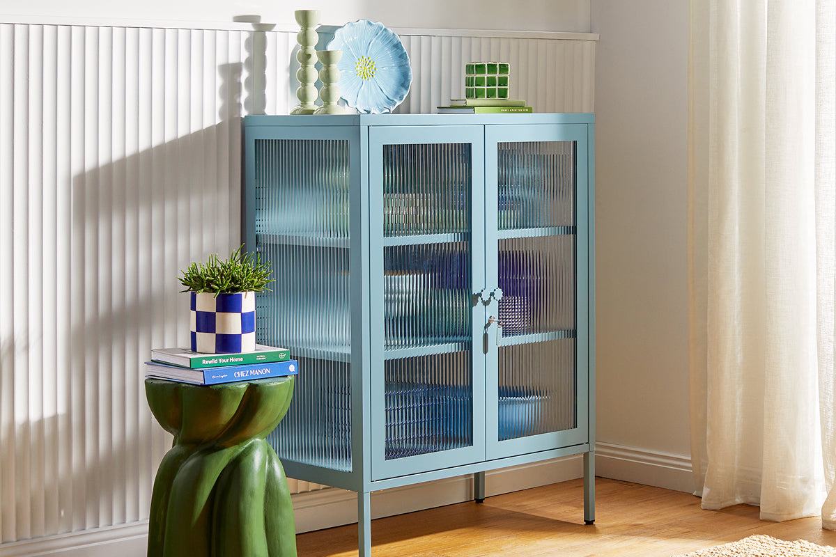 Mustard Made's The Mixer glass cabinet in Ocean, a pale dusty blue, styled with ceramics against fluted wall paneling