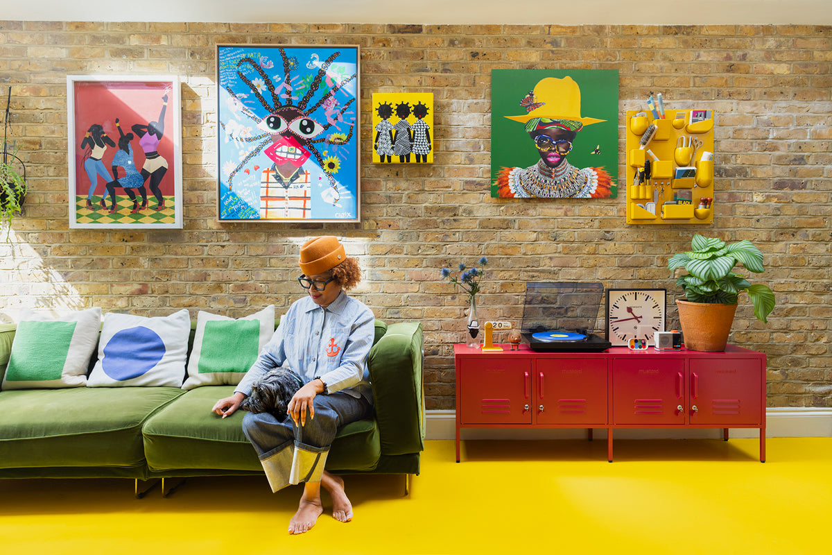 Natasha Landers on a green velvet sofa under a brick wall gallery of colorful art, beside Poppy red lockers on a yellow floor