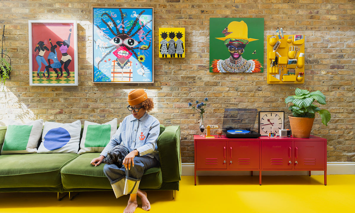 Natasha Landers on a green velvet sofa under a brick wall gallery of colorful art, beside Poppy red lockers on a yellow floor