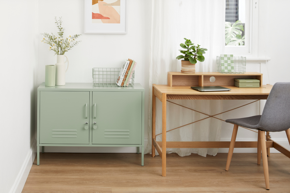 A Sage Lowdown locker sits in a home office next to a wooden desk with a chair. There is a laptop on the desk and small potted plants and books decorating the space.