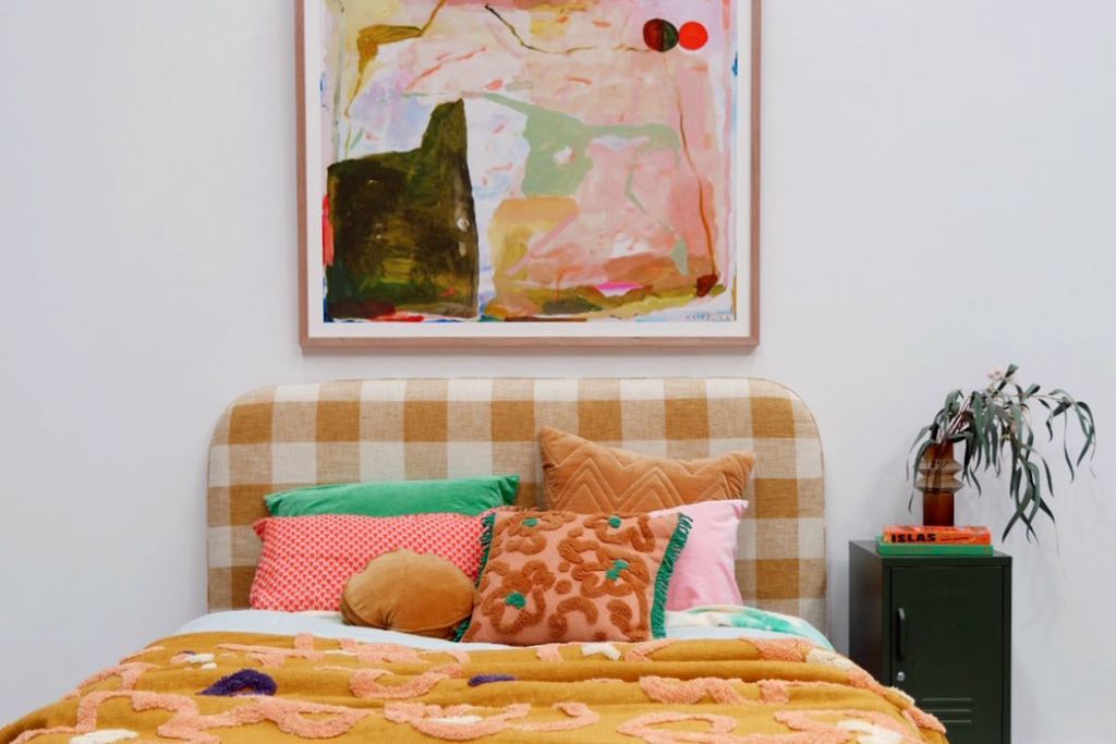 Colorful artwork hanging above a bed, a Mustard Made locker is beside the bed.