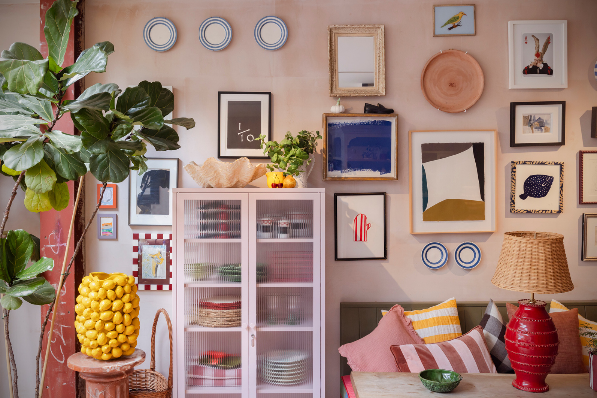 A Blush pink locker with glass doors against a pink wall filled with an eclectic mix of framed artworks, plants, cushions and other decor items.