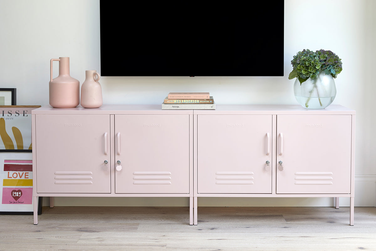 A pair of The Lowdown lockers in Blush pale pink beneath a wall-mounted TV, styled with vases, books and a leafy plant