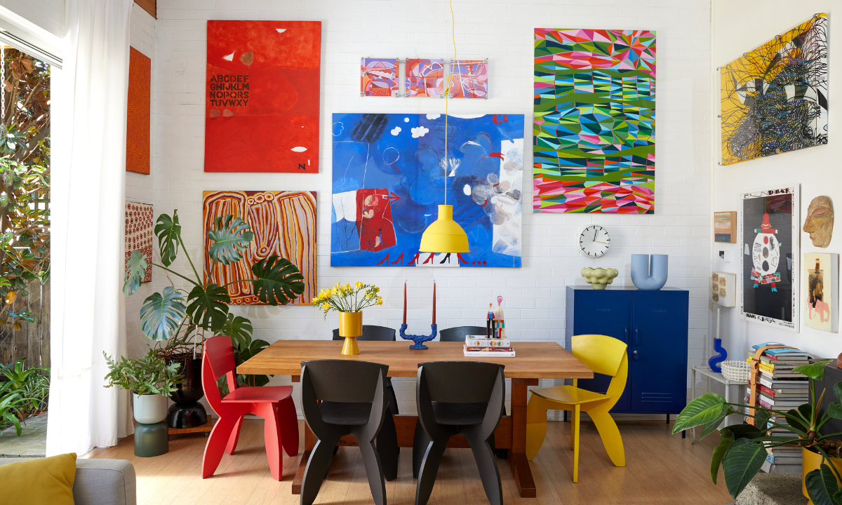 A colorful dining room featuring white brick walls, large abstract paintings and quirky chairs in red, black and yellow.