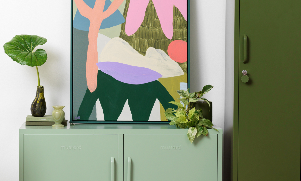 A brightly coloured print sits on top of a Sage Lowdown locker in a room filled with plants.