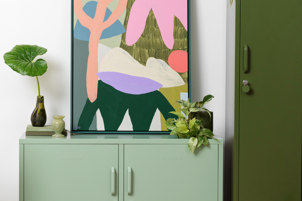 A brightly coloured print sits on top of a Sage Lowdown locker in a room filled with plants.
