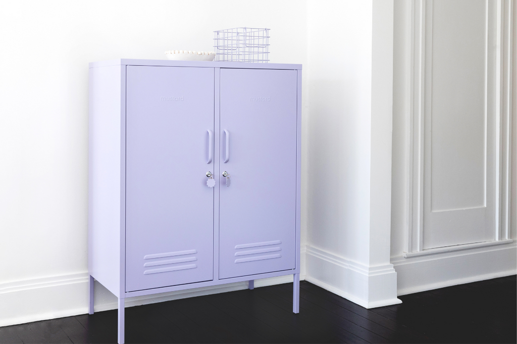 A Lilac Midi locker sits against a white wall with dark wood floors. There is a Lilac Basket and a small white bowl styled on top.