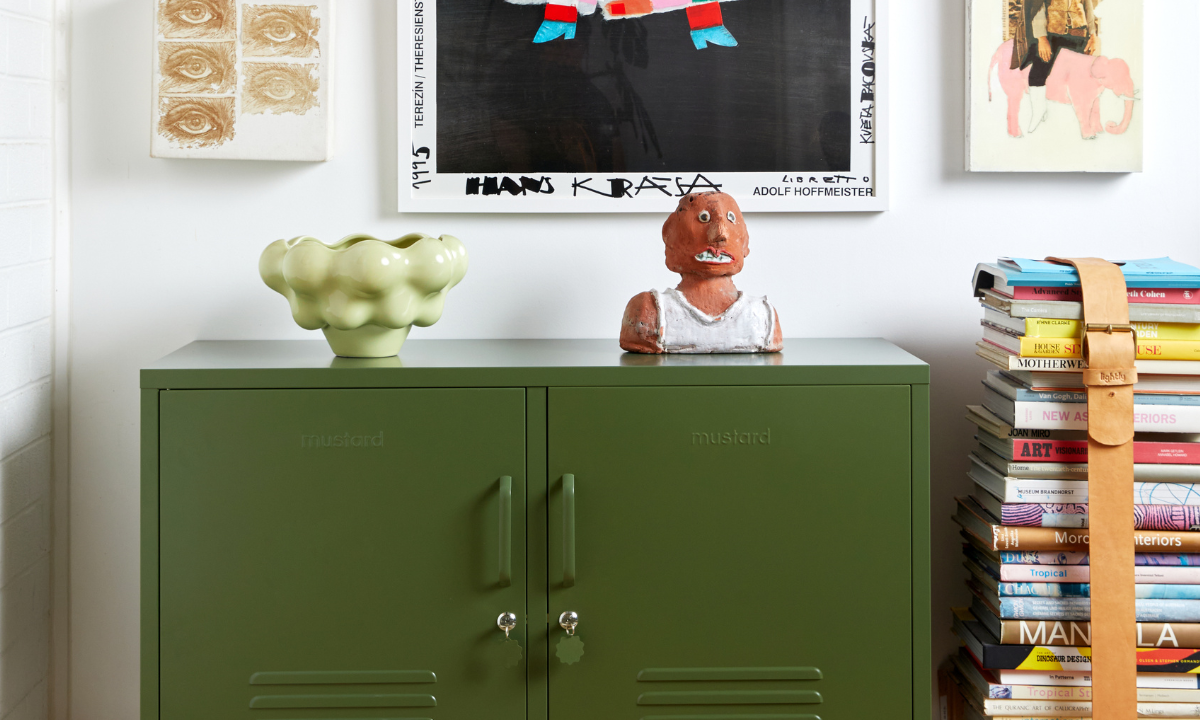 An Olive Lowdown Mustard Made Locker is styled next to a stack of coffee table books and an eclectic range of colorful artworks.