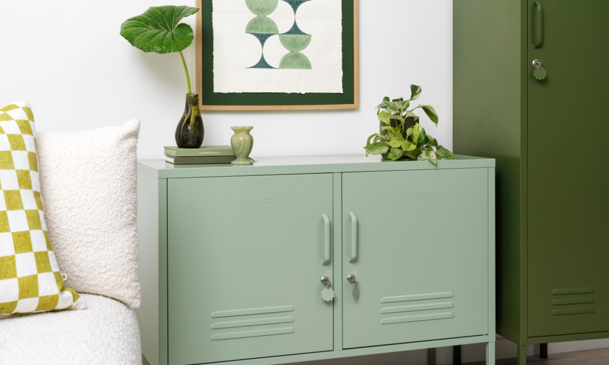 A Sage Lowdown sits next to an Olive Skinny locker. They are accessorized with leafy green plants, some green books and an artwork in shades of green.