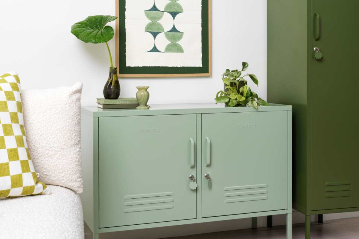A Sage Lowdown sits next to an Olive Skinny locker. They are accessorized with leafy green plants, some green books and an artwork in shades of green.